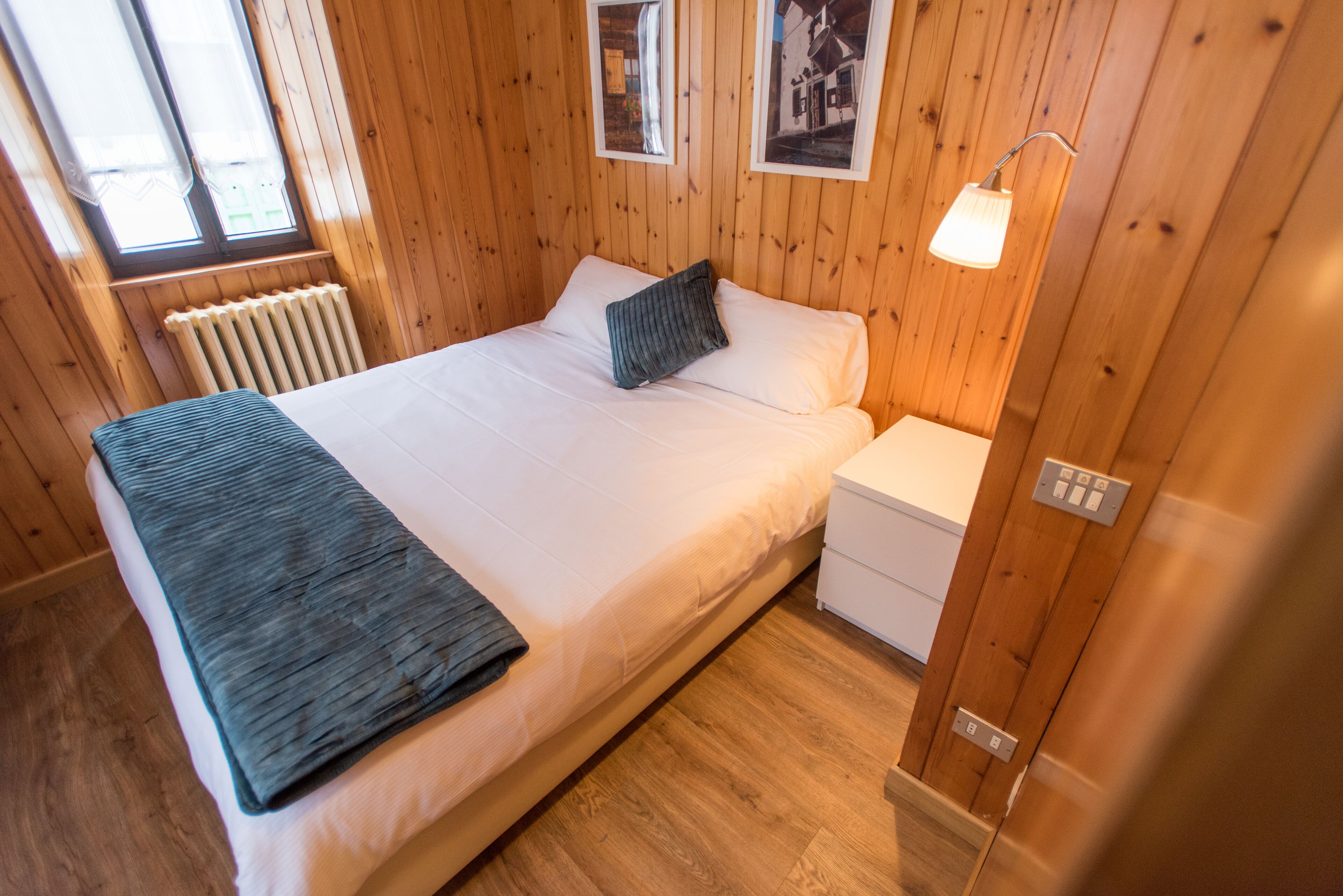 Un dormitorio con paneles de madera, una cama, una mesita de noche, una lámpara y un radiador.