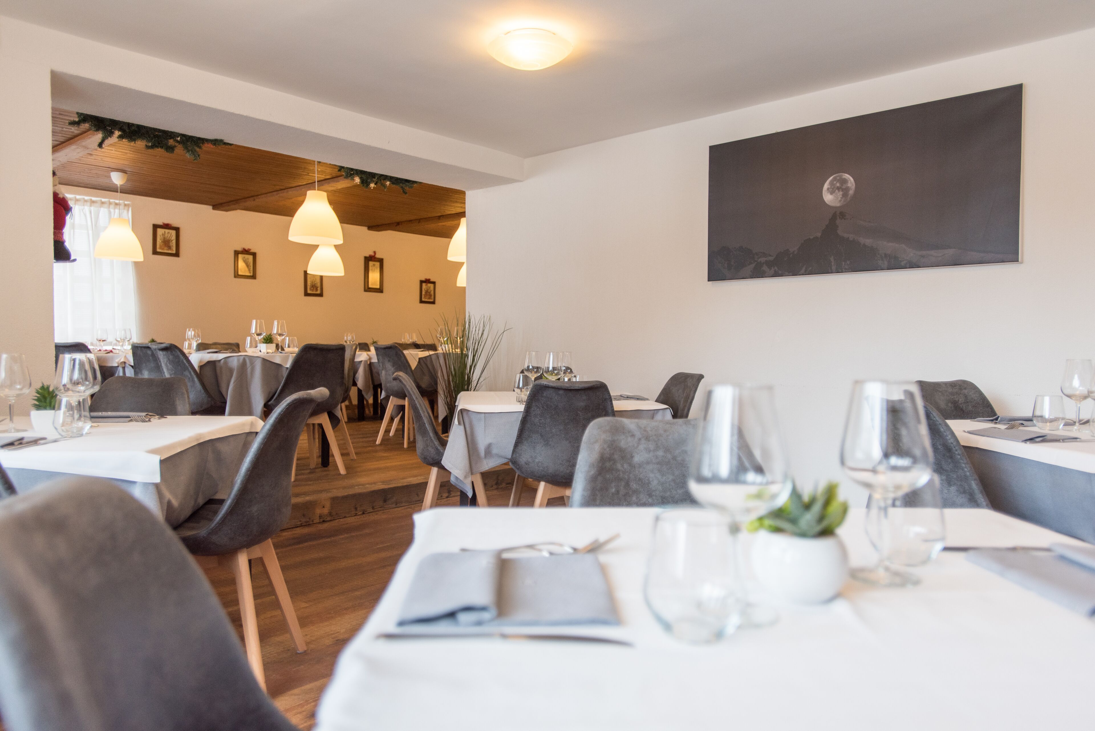 A restaurant with tables set for dining, chairs, and hanging pendant lights.