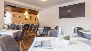 A restaurant with tables set for dining, chairs, and hanging pendant lights.