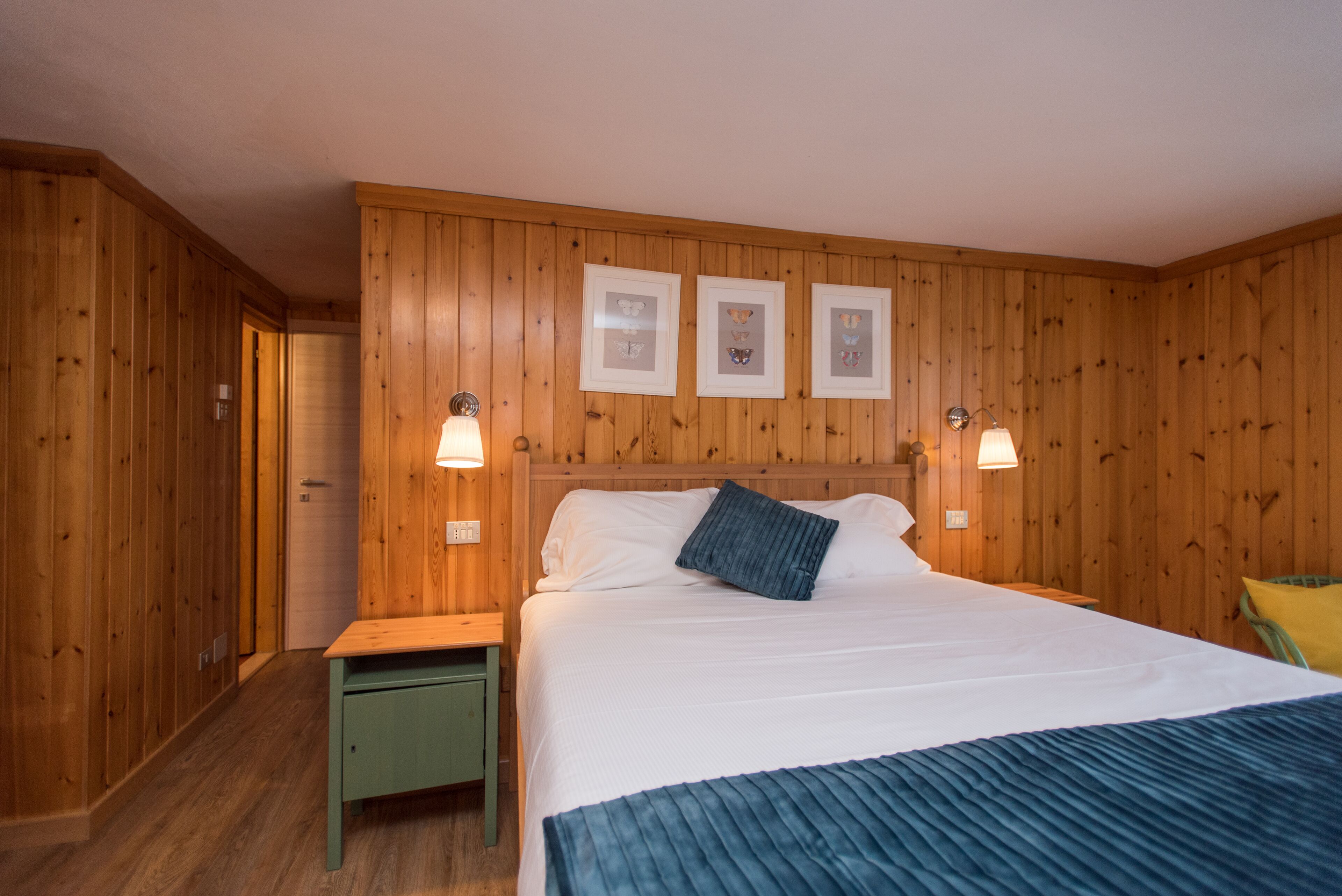 Ein Zimmer mit Holzwänden, einem Bett, zwei Nachttischen und Wandleuchten.