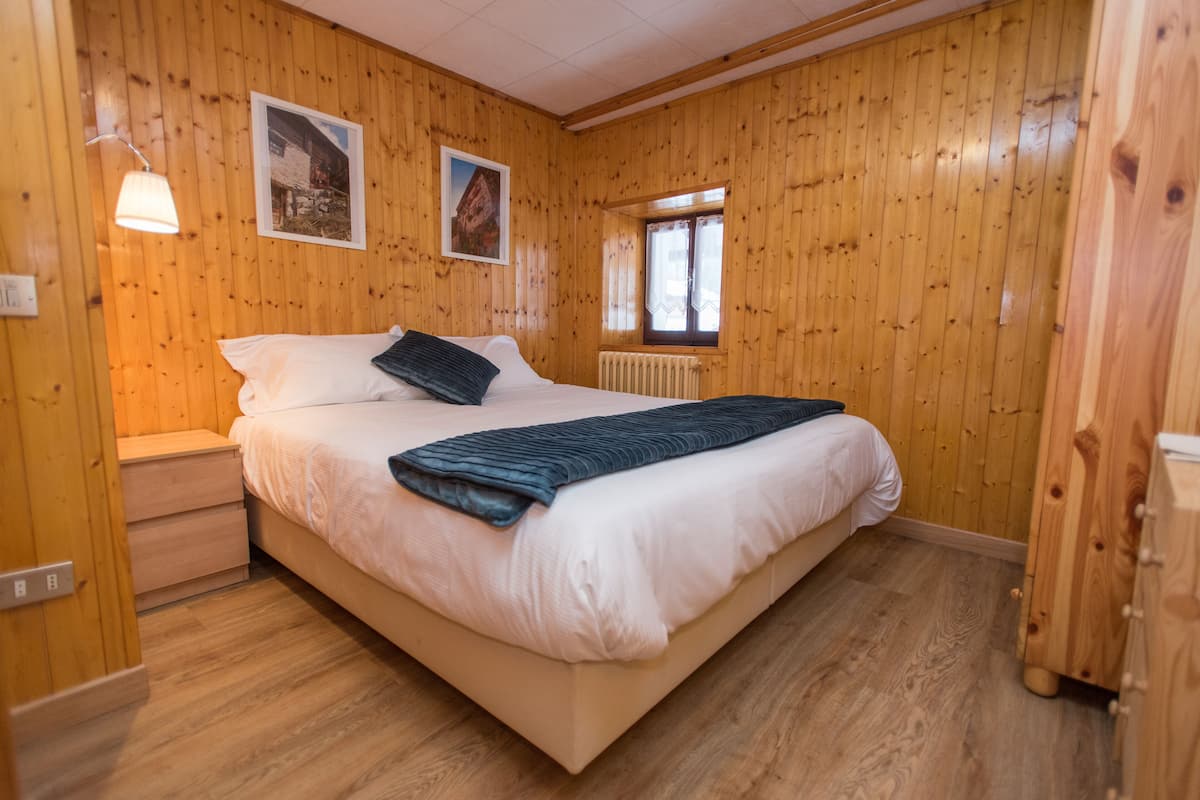 A wooden-paneled room with a bed, a nightstand, a lamp, and two framed pictures on the wall.