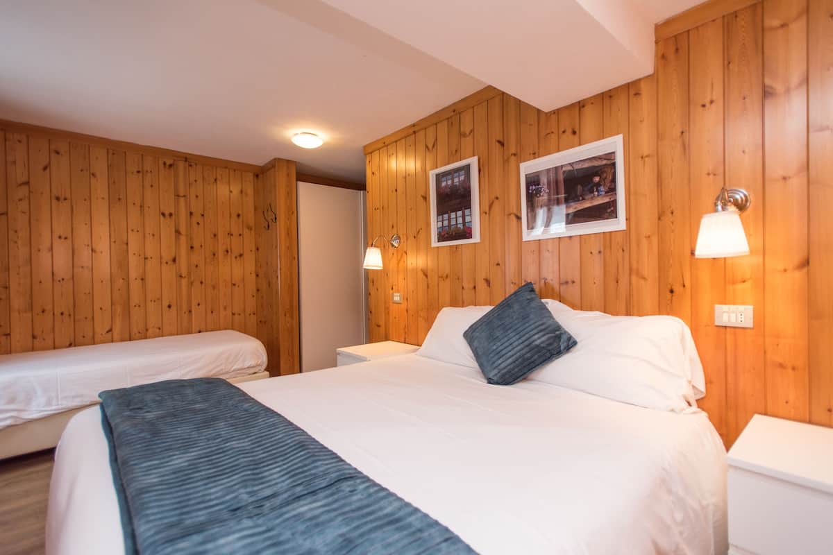 A room with wooden panel walls, two beds with white bedding, and wall-mounted lamps.