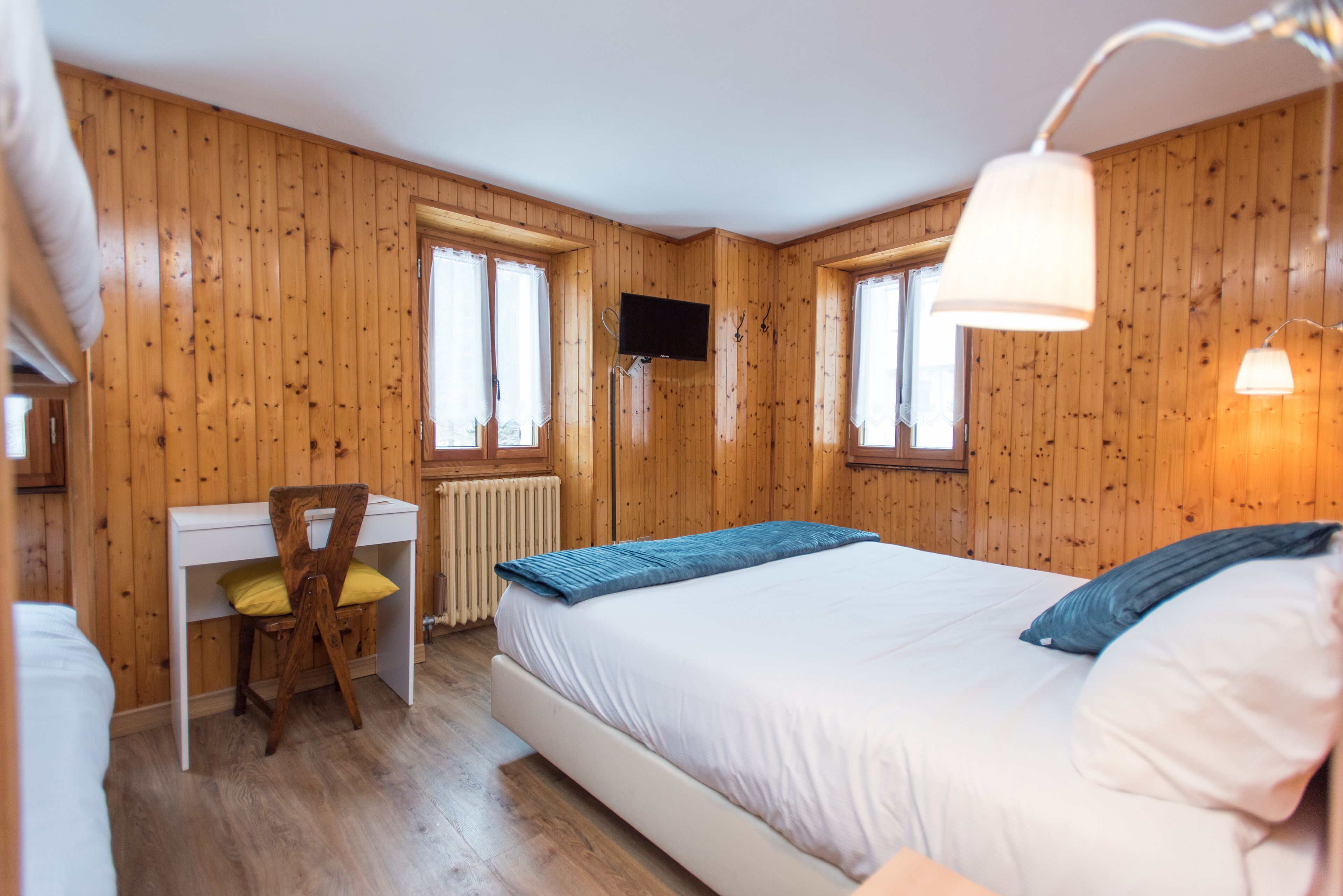 A wooden-paneled room with a bed, a desk, and a TV.