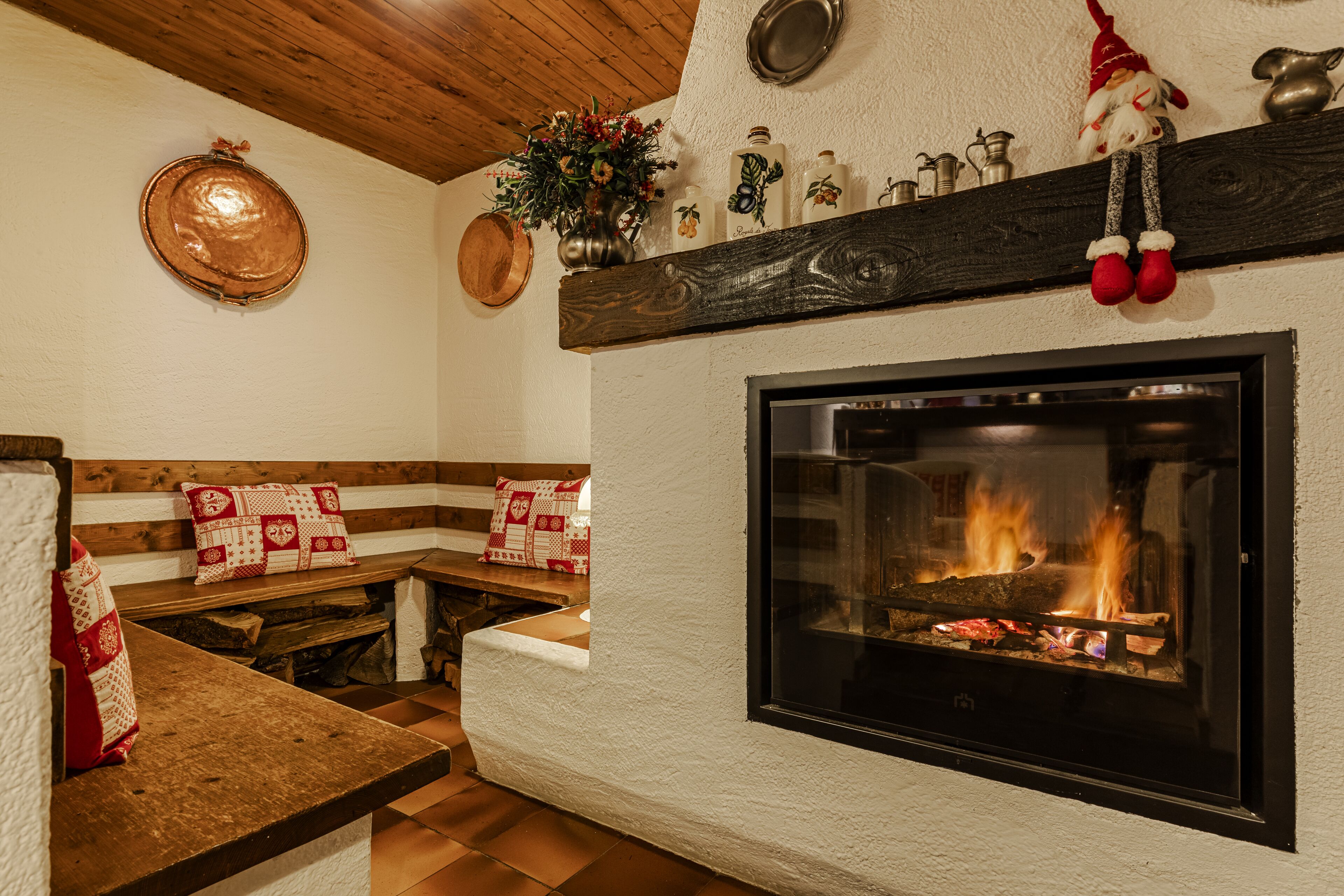 Una chimenea acogedora con un alero adornado con diversos objetos, un banco con cojines estampados y un techo de madera.