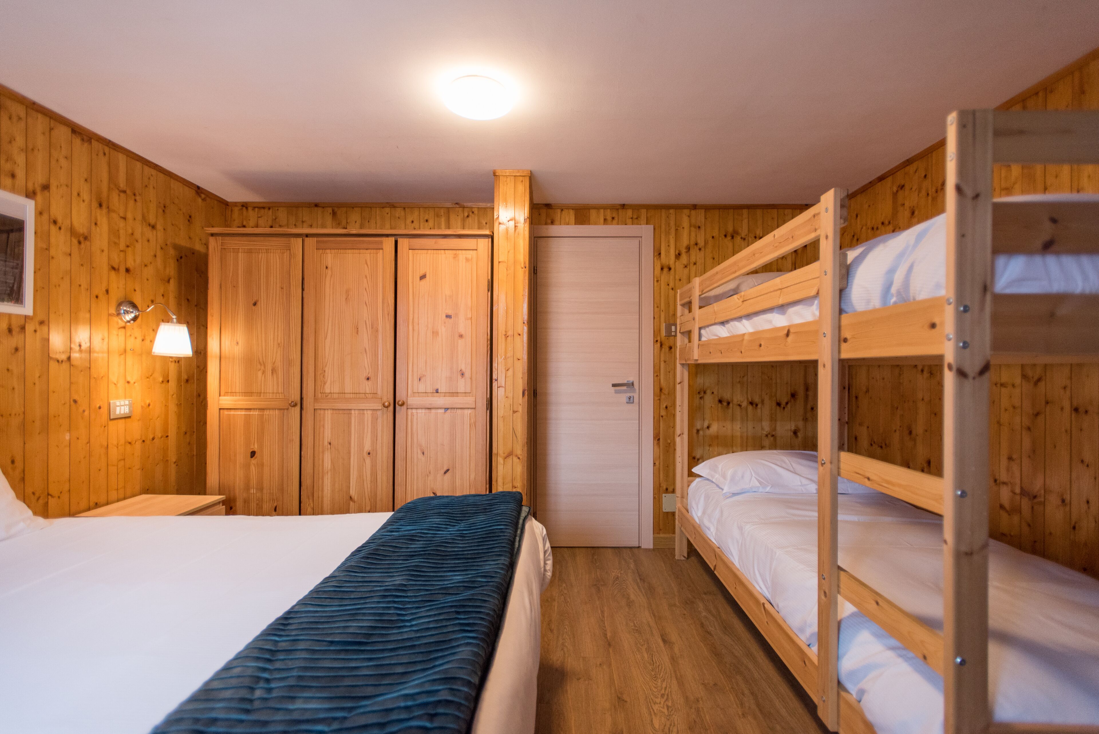 Quarto de madeira com beliches, uma cama de solteiro e um guarda-roupa.