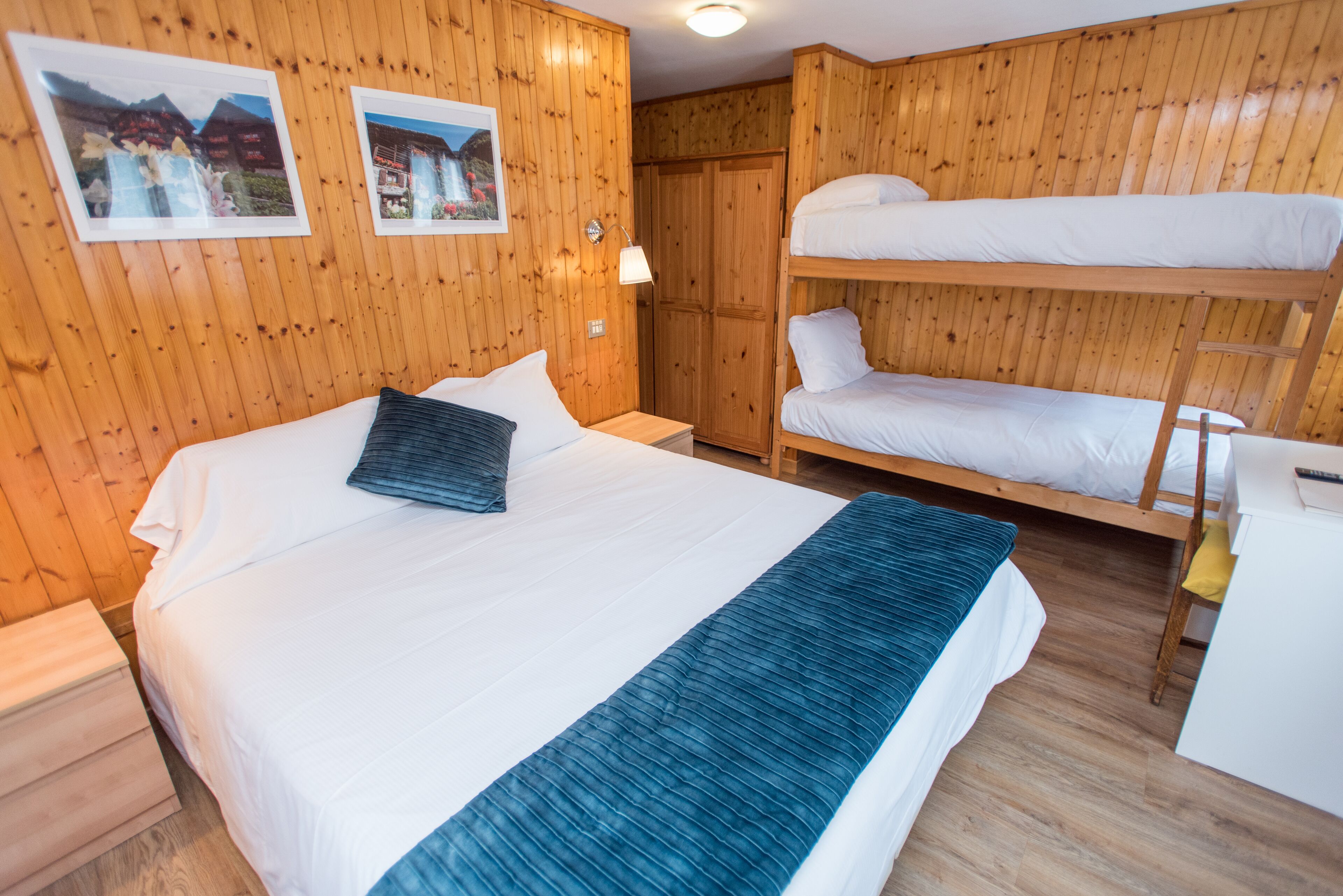 A wooden-paneled room with a bunk bed, a single bed, and a desk.
