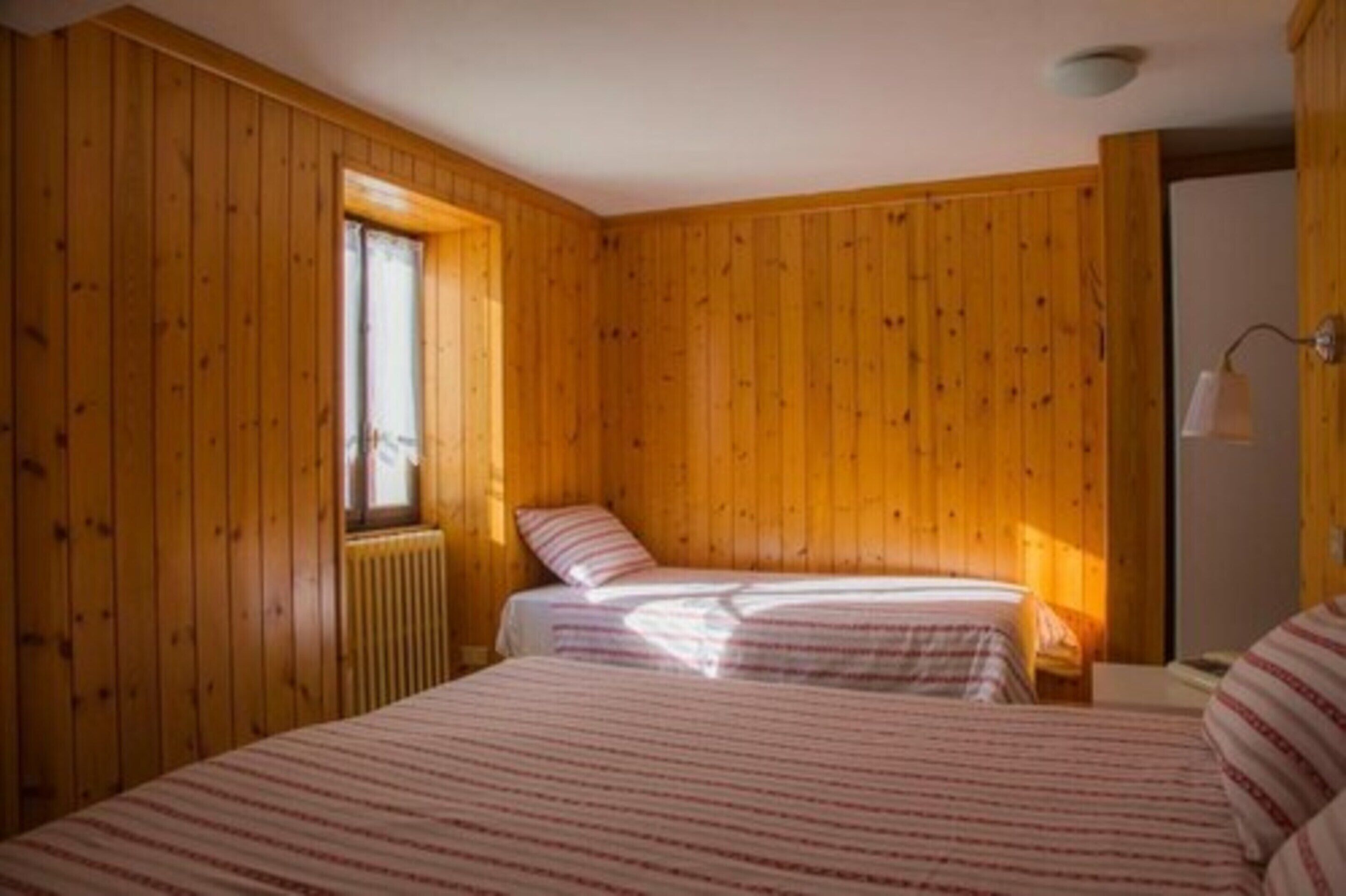 A wooden-paneled room with two beds, a window, and a radiator.