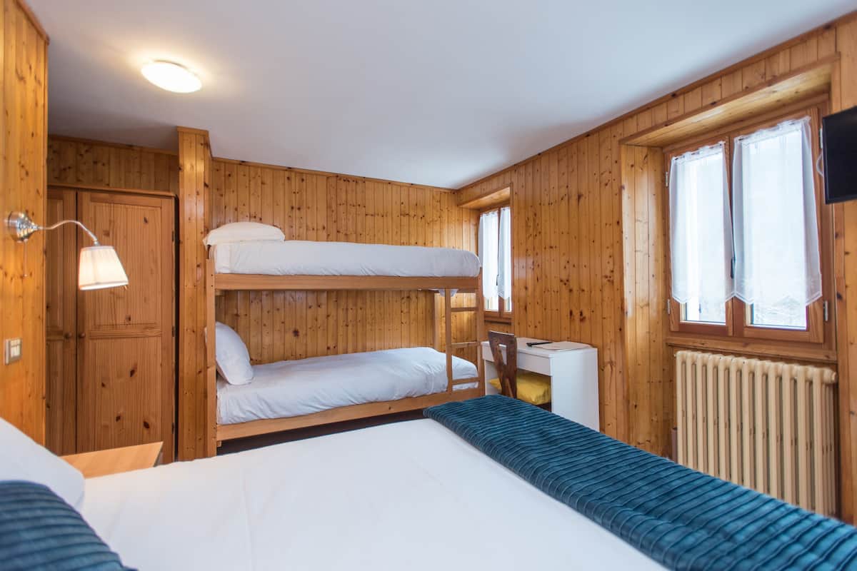 A bunk bed room with a desk and chair, wooden walls, and a window with curtains.