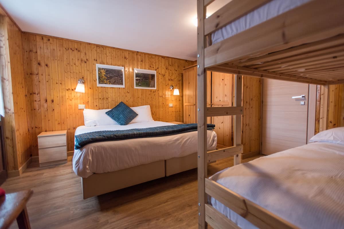 A wooden-paneled room with a bunk bed, a bedside table, and two wall-mounted lamps.