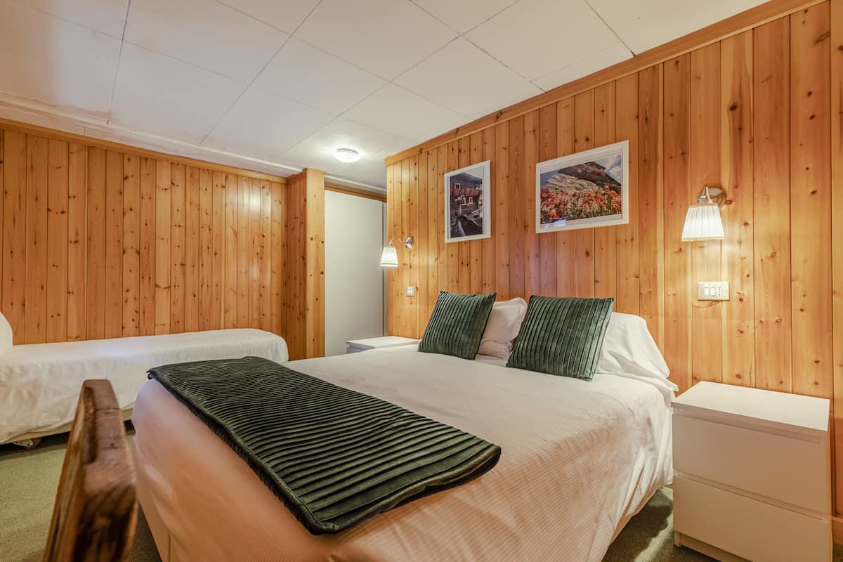 A hotel room with wooden panel walls, two beds, a nightstand, a lamp, and two framed pictures.