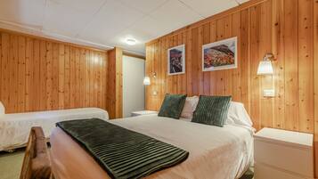 Habitación de hotel con paredes de paneles de madera, dos camas, una mesita de noche, una lámpara y dos cuadros enmarcados.