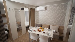 Una habitación compacta con una mesa de comedor preparada para dos personas, un sofá y una pequeña zona de kitchenette.