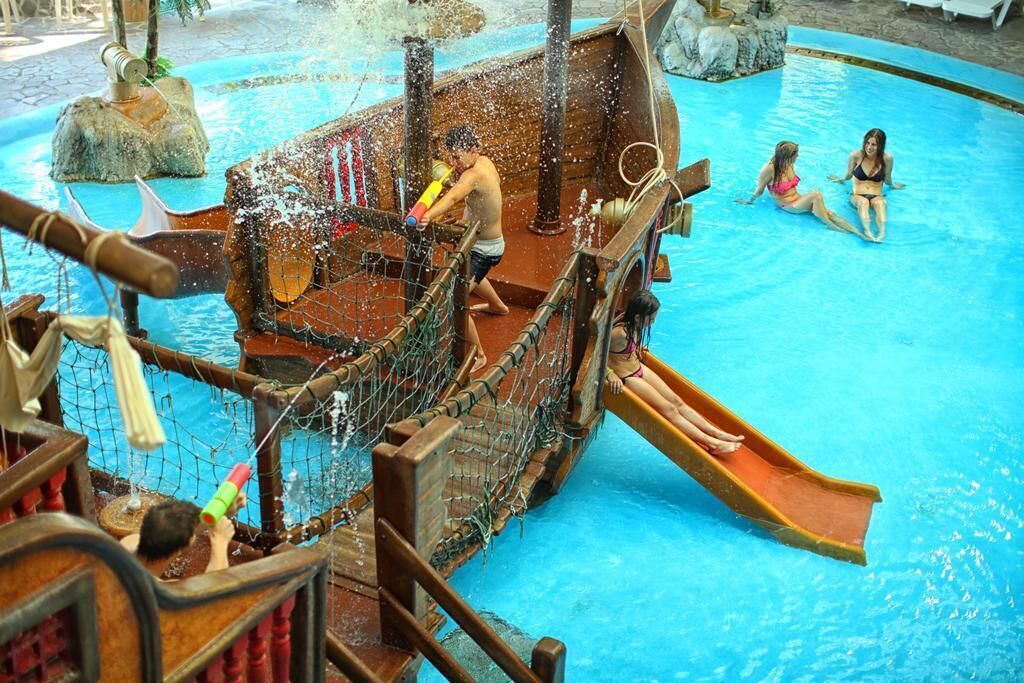 A pool with a wooden ship structure and a slide.