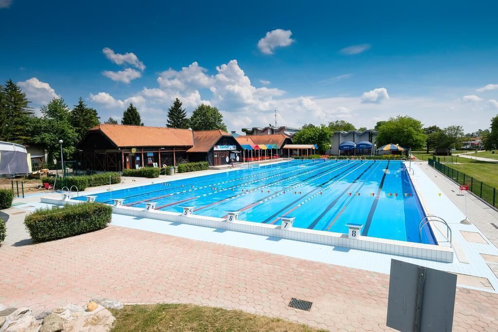 Una amplia piscina al aire libre con varias pistas de natación, rodeada de edificios y vegetación.