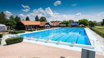 Una amplia piscina al aire libre con varias pistas de natación, rodeada de edificios y vegetación.