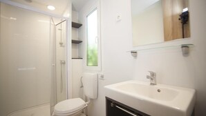Un baño con ducha de mampara de vidrio, inodoro blanco, lavabo con espejo y ventana.