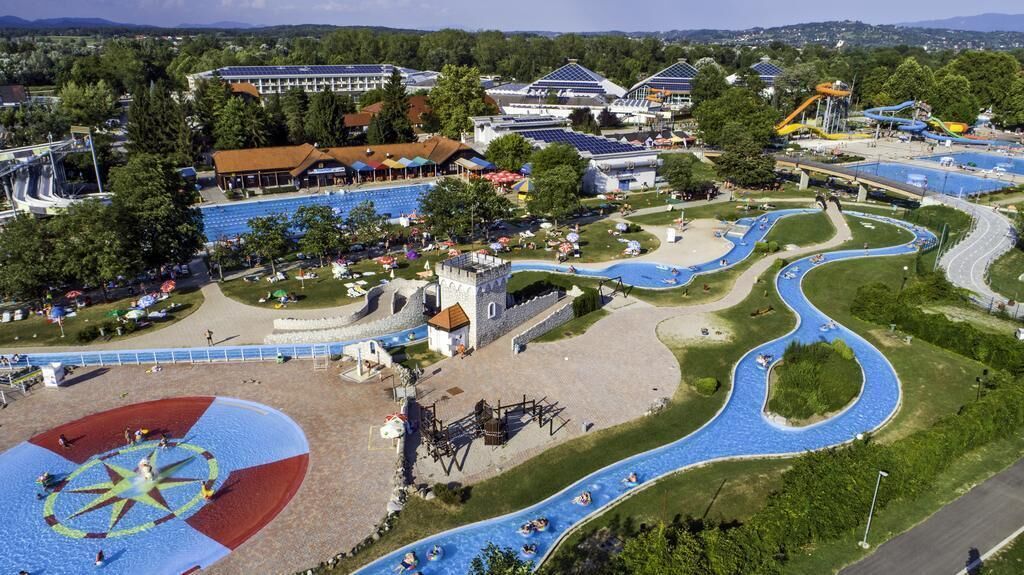 Vue aérienne d’un parc aquatique avec un toboggan sinueux, une grande piscine et une structure ressemblant à un château.