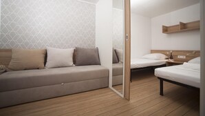 Una habitación moderna con sofá, dos camas individuales, suelo de madera y pared con estampado geométrico.