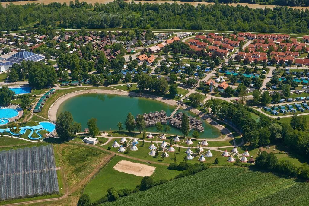 An aerial view of a resort with a large lake, multiple bungalow-style accommodations, and a solar panel array.