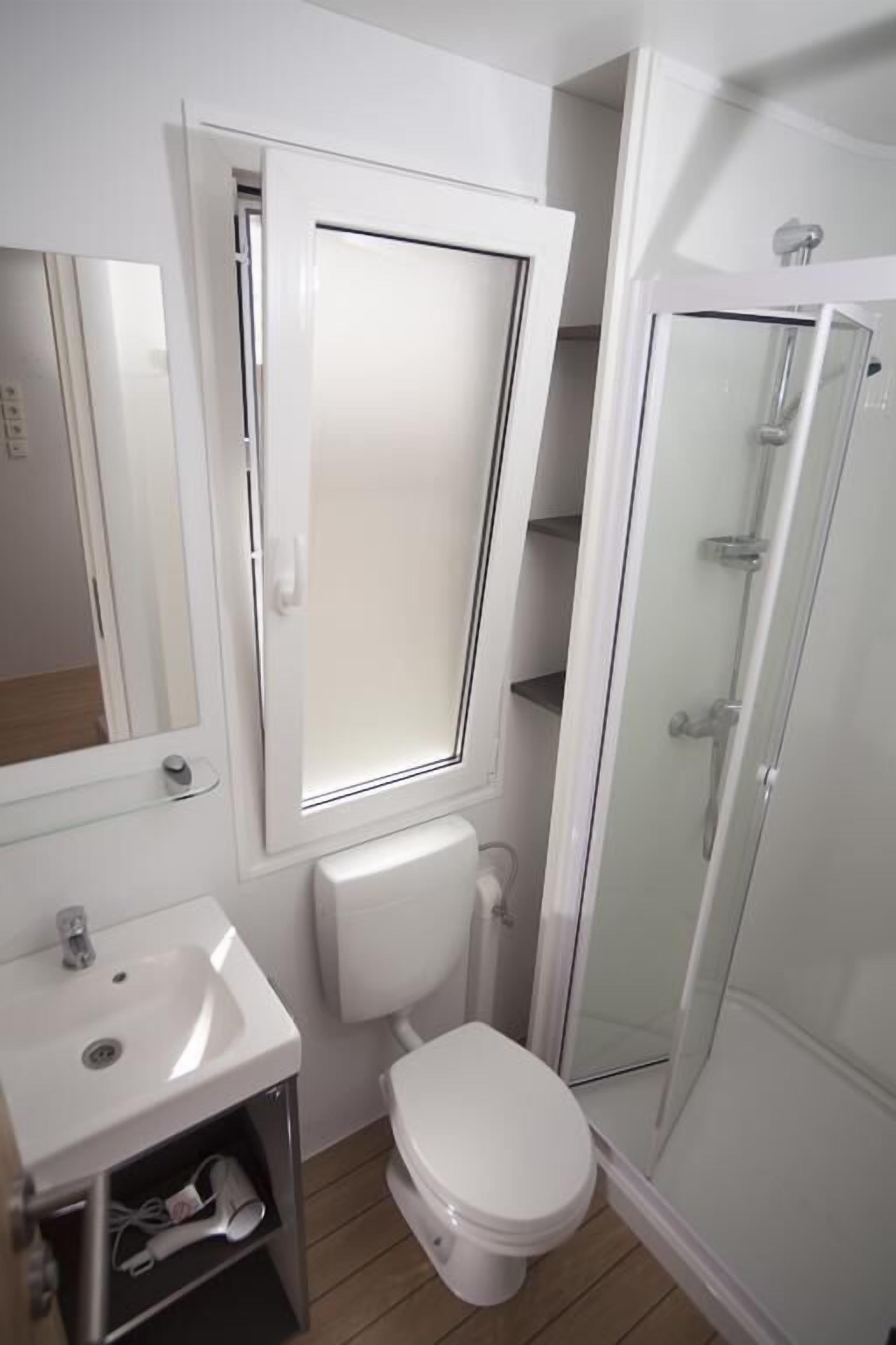 A bathroom with a toilet, a sink, a mirror, and a glass-enclosed shower.