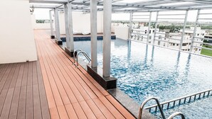A wooden deck with a pool, metal railings, and a view of buildings in the background.