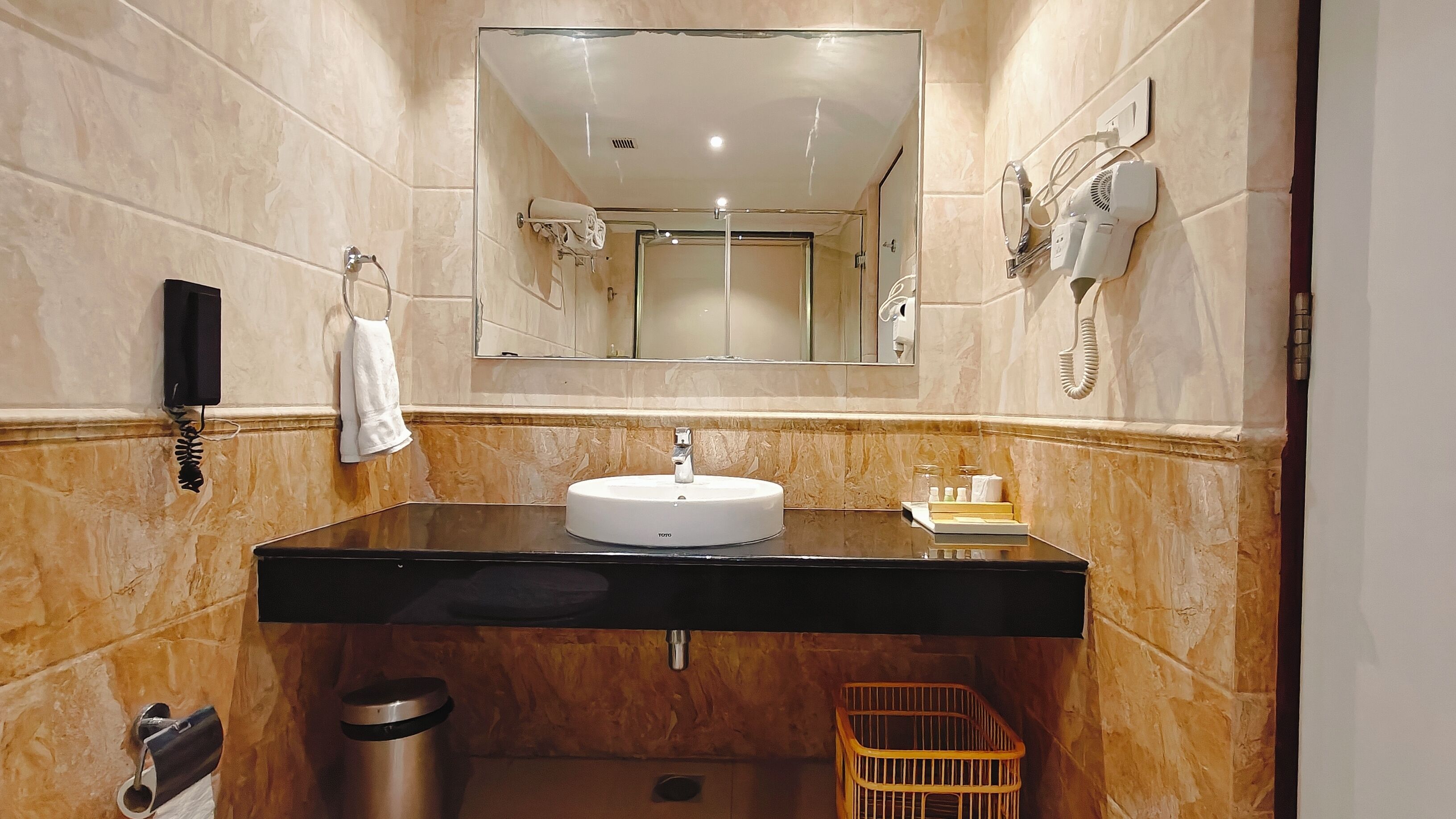 Casa de banho com lavatório preto, espelho, porta-toalhas, secador de cabelo e um cesto de lixo.