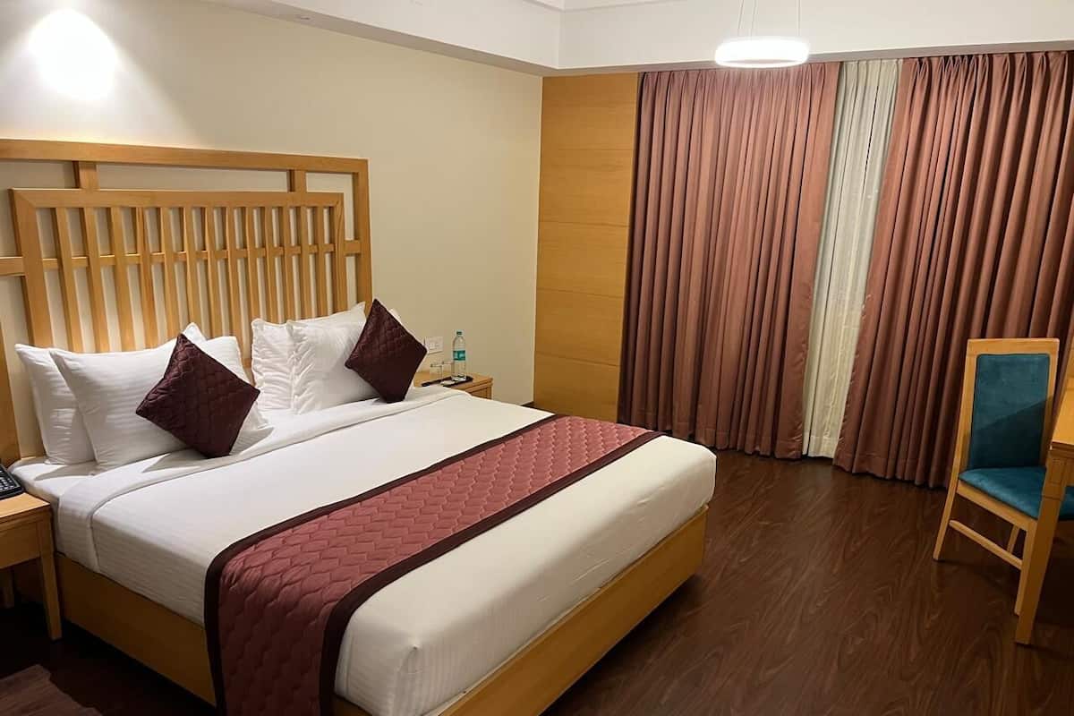 Habitación de hotel con una cama de madera, una mesita de noche, una silla y un ventanal con cortinas.