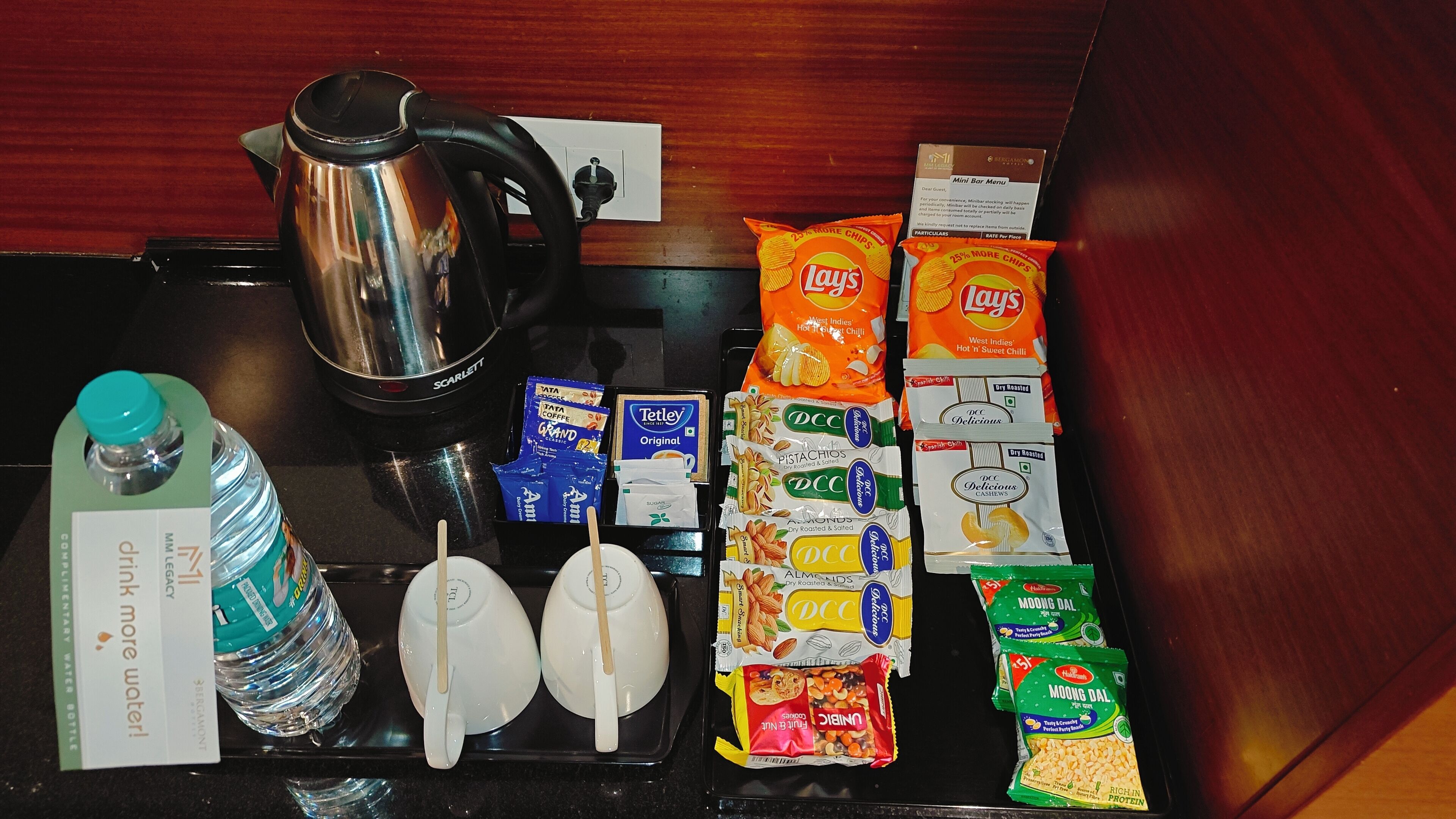 A kitchen counter with a kettle, water bottle, tea bags, coffee packets, and various snacks.