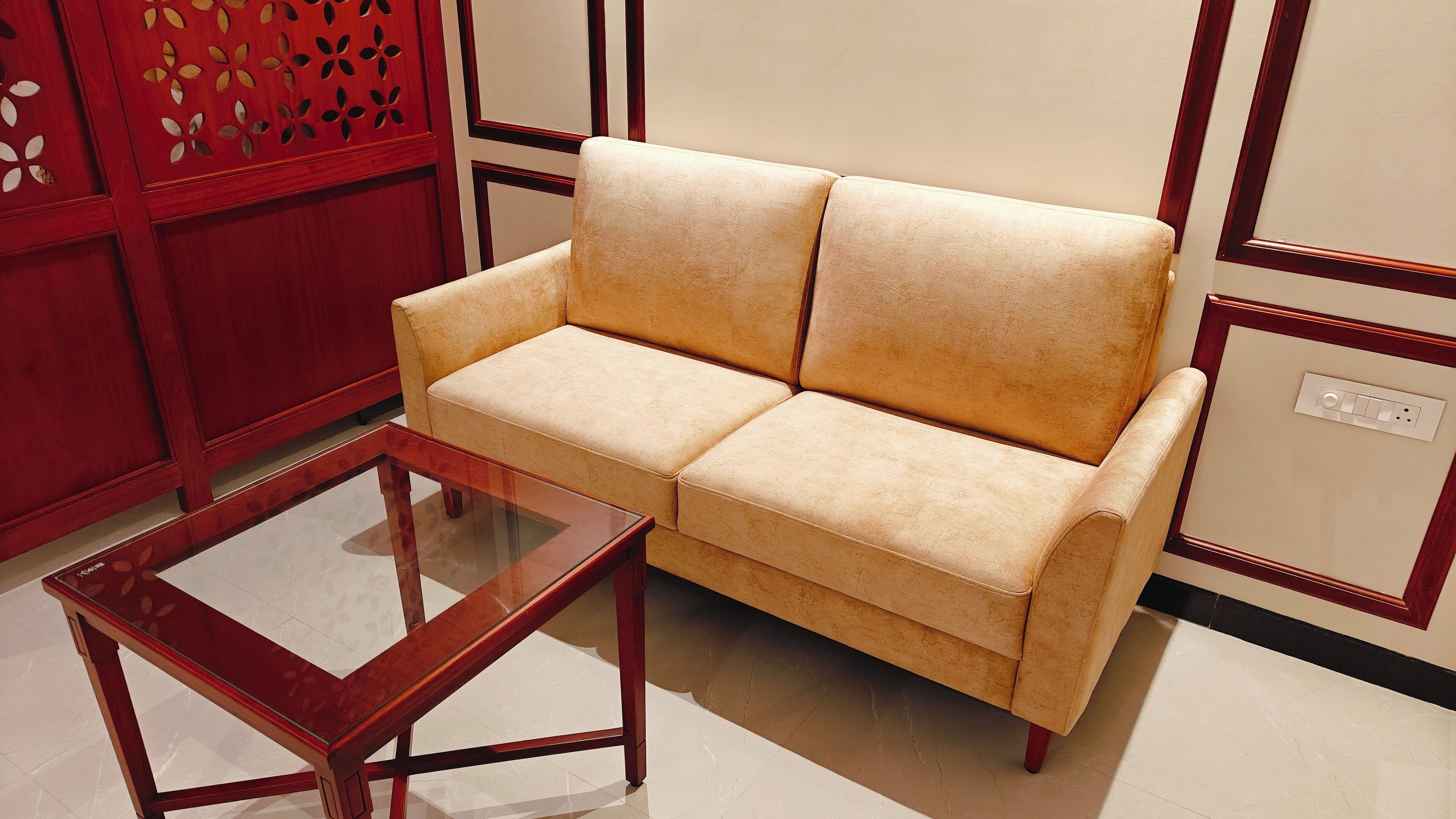 Un divano beige con struttura in legno, un tavolino da caffè in vetro e un mobiletto rosso anch'esso in legno, decorato con intagli.