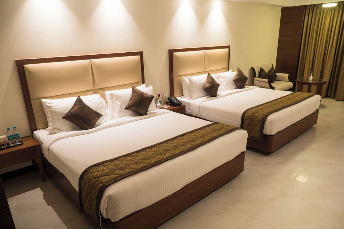 Habitación de hotel con dos camas, cada una con cabecero, almohadas y una manta. Hay una mesita de noche con un teléfono y botellas de agua.