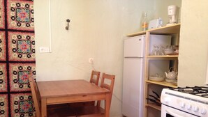 A compact kitchen with a wooden table and chairs, a white refrigerator, a stove, and a shelf with kitchenware. - cottage: nature and lavender (la rochette du buis)