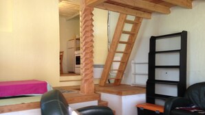 A compact living space with a loft area, a wooden ladder, a black chair, a glass table, and a pink bedspread. - cottage: nature and lavender (la rochette du buis)