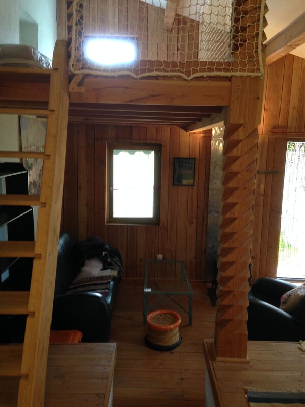 A wooden interior with a loft bed, a small table, and a window.