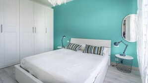 A bedroom with a white bed, teal walls, a white wardrobe, and a round mirror. - GuestHost - Annika's House - Lagoon View and Private Parking (Grado)