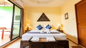A hotel room with a bed, two bedside tables, a ceiling fan, an air conditioning unit, a sliding glass door, and a wooden door. - Chang Charlie Inn (Pattaya)
