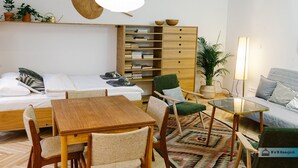 A modern, well-lit room with a bed, a wooden table with chairs, a green armchair, a sofa, a bookshelf, and a potted plant. - Warsaw Concierge Saska Studio (Warsaw)