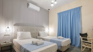 A hotel room with two beds, a bedside table with a lamp, a chair, and a large window with blue curtains.