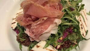 A plate with a salad, prosciutto, and grilled cheese slices.