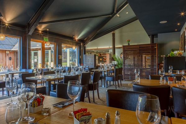 Enjoy dining in a stylish restaurant with wooden tables, black chairs, and large windows offering a view of the outdoor area.