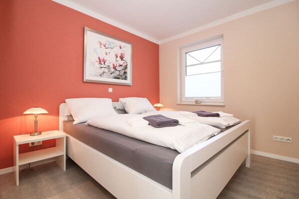 Un dormitorio con cama, dos mesitas de noche, una ventana y un cuadro en la pared.