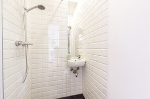 A bathroom with white tiled walls, a shower, and a sink with a mirror. - Warsaw Concierge Studio Old Town Square (Warsaw)
