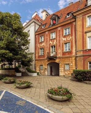 A courtyard with a building featuring a red facade and a balcony. There are flower planters and a blue bike lane. - Warsaw Concierge Studio Old Town Square (Warsaw)