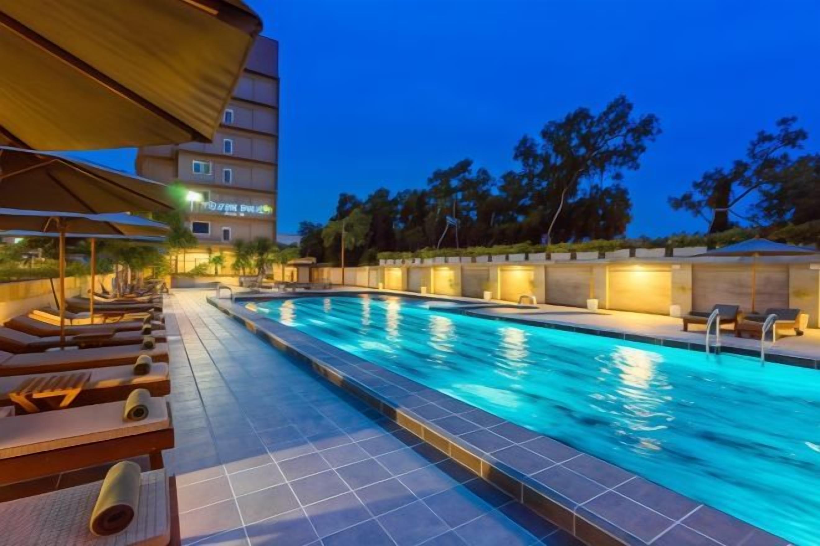 Una piscina con sillas de descanso y sombrillas, rodeada por un edificio con un letrero.