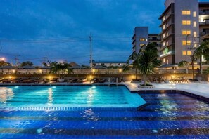 A swimming pool with lounge chairs and a building with multiple floors and windows. - Olive Tree Hotel Pattaya (Sattahip)