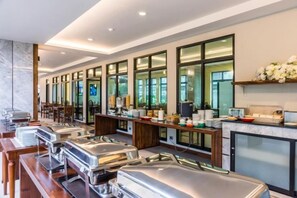 A buffet area with stainless steel chafing dishes, a long counter, and a fireplace. - Olive Tree Hotel Pattaya (Sattahip)