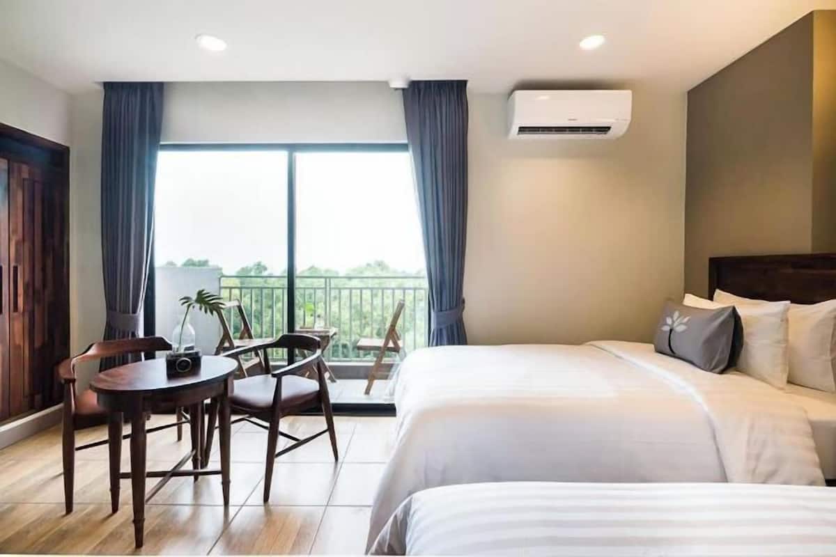 A hotel room with a bed, a table with chairs, a balcony view, and an air conditioning unit.