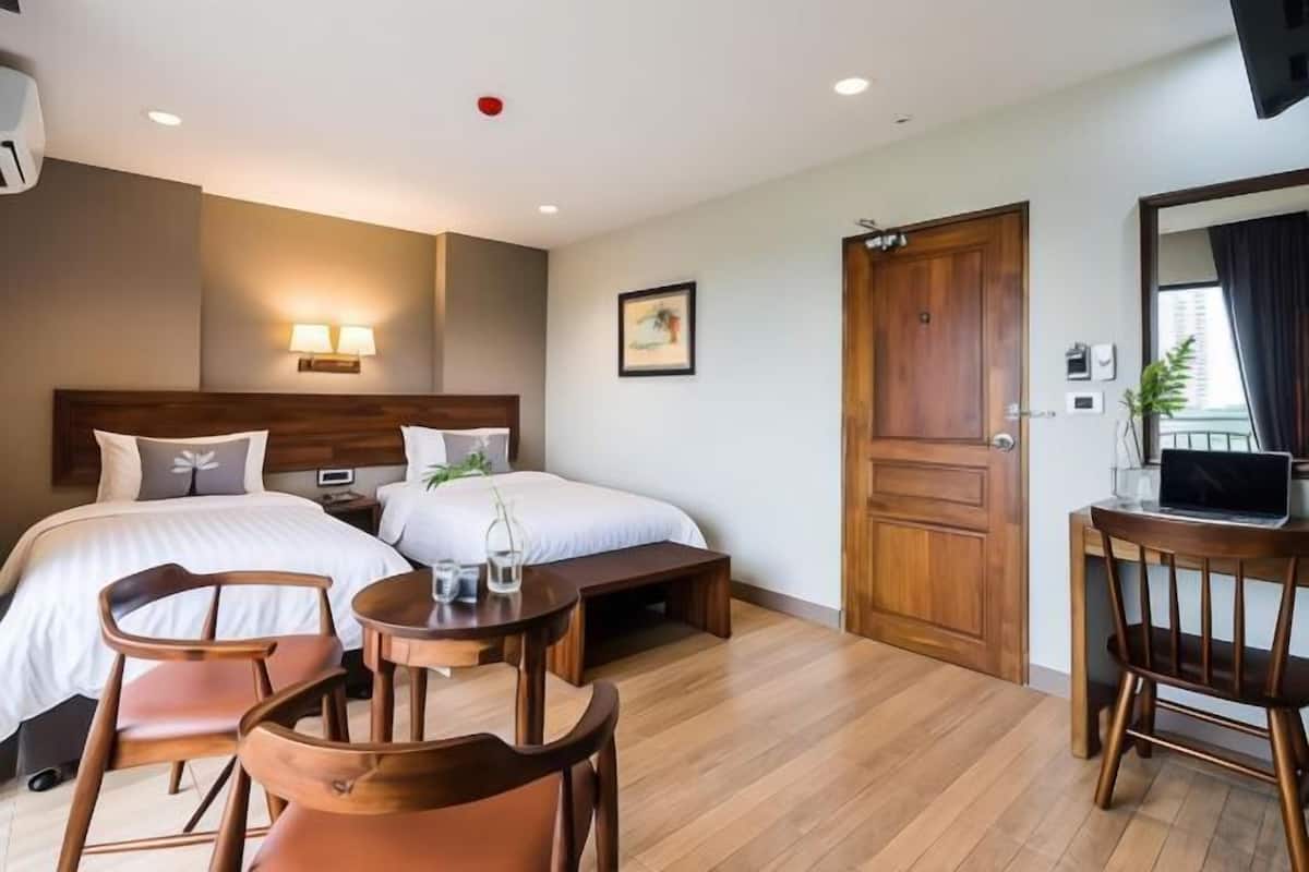 A hotel room with two beds, a desk with a chair, a small table, and a TV.
