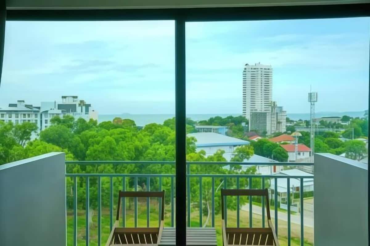 A balcony with two wooden chairs, a view of a cityscape with buildings and greenery, and a clear sky.