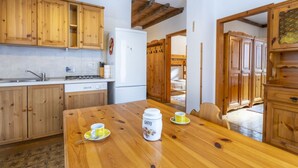 Eine Küche mit Holzschränken, einem weißen Kühlschrank und einem Esstisch mit gelben Tassen und einer Kaffeekanne.