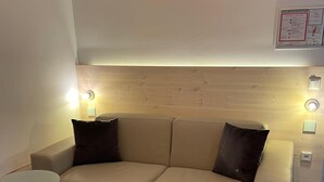 Un sofá de tonos neutros con dos cojines oscuros, una mesita redonda y un cabecero de madera.